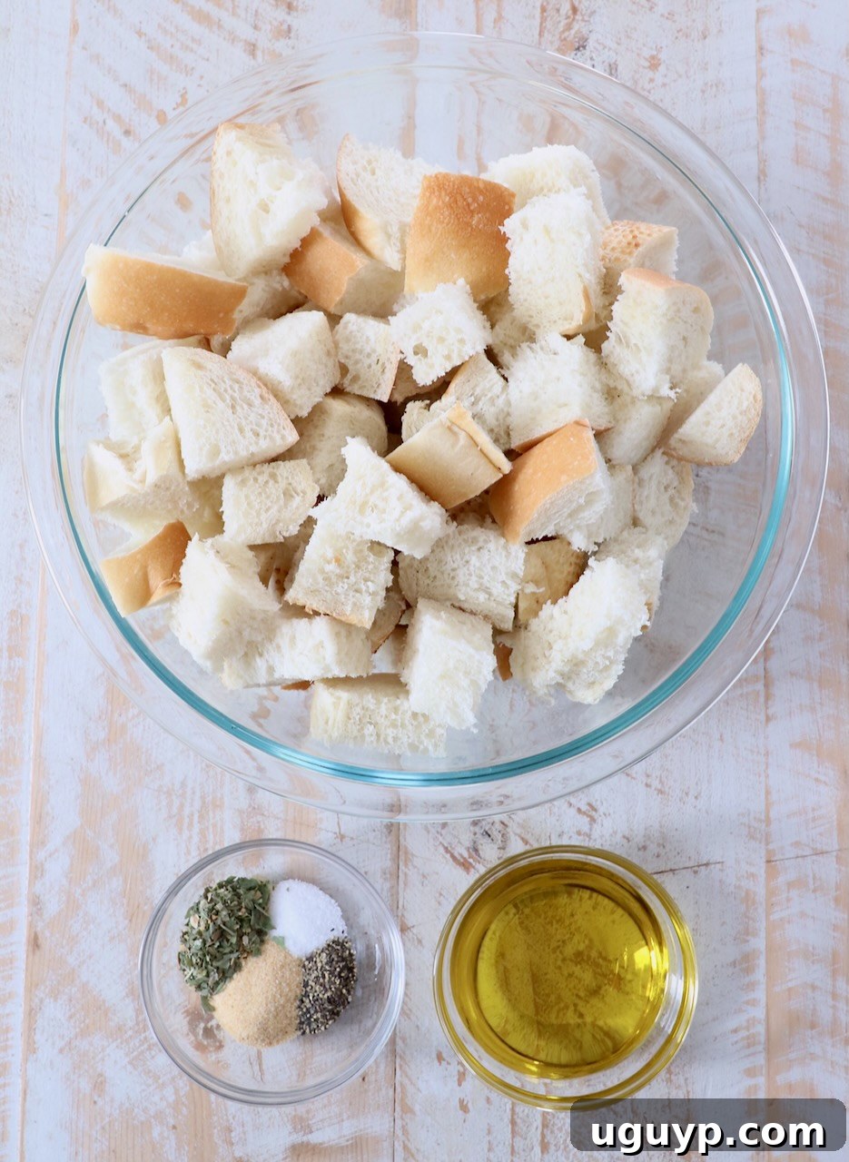 Ingredients for homemade croutons laid out on a white wooden board, including cubed bread, olive oil, and various spices.