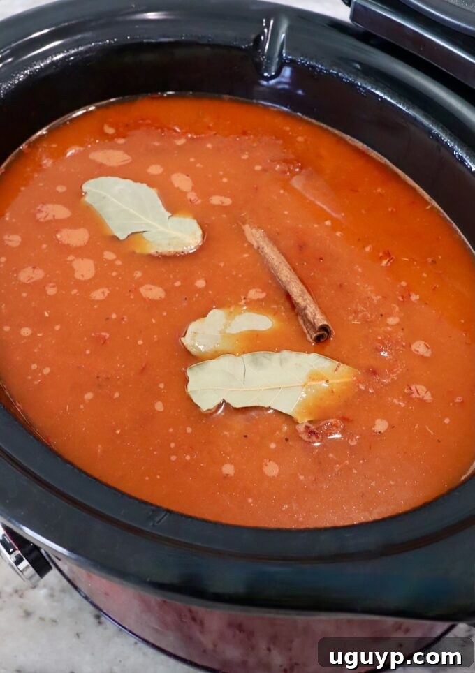 chili tomato sauce in slow cooker topped with bay leaves and cinnamon stick