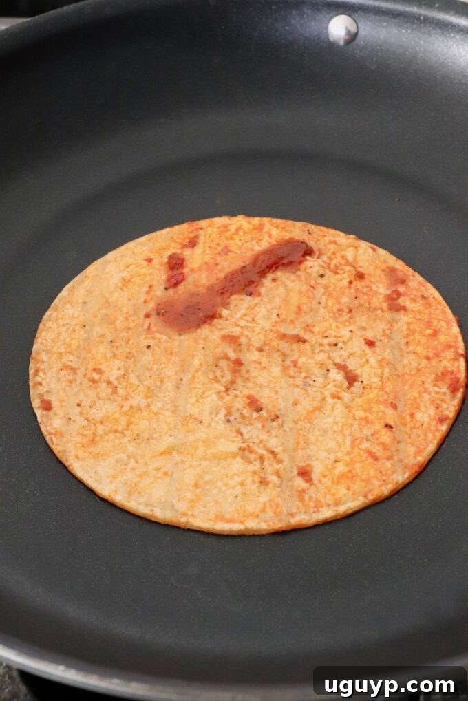 tortilla dipped in sauce in skillet