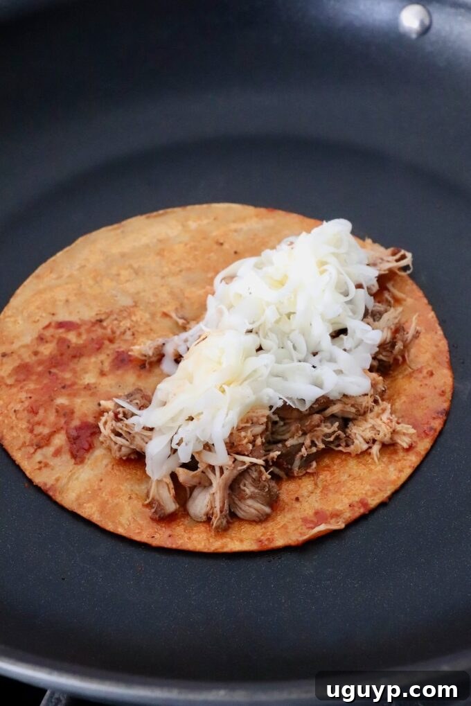 tortilla topped with shredded chicken and cheese in skillet