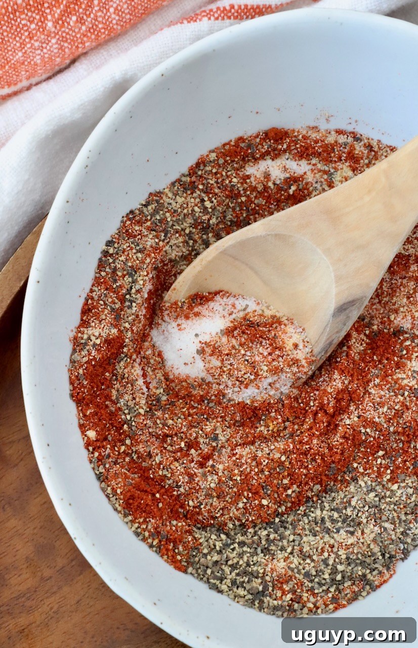 A close-up shot of various spices perfectly mixed together in a bowl, with a wooden spoon, showcasing the rich texture and vibrant colors of the homemade burger seasoning.
