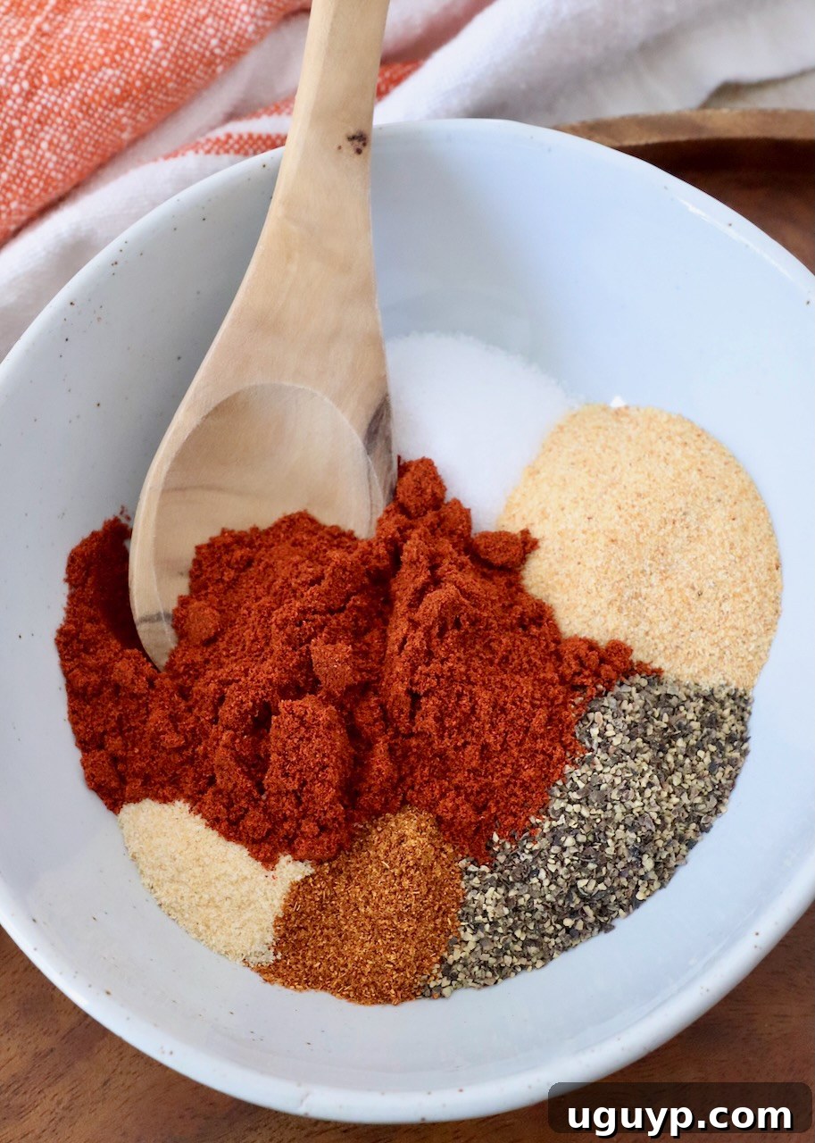 A bowl artfully arranged with separated spices before mixing, alongside a wooden spoon, symbolizing the careful selection of ingredients for the best homemade hamburger seasoning.