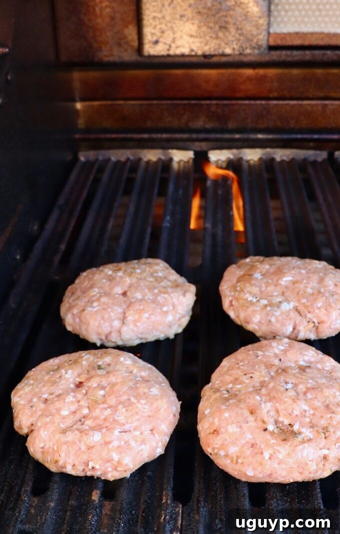 Uncooked turkey burger patties sizzling on a hot grill