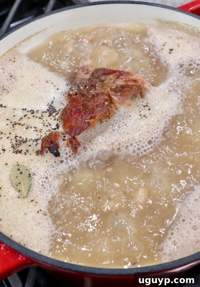 The pinto beans and ham hock simmering gently in the flavorful liquid on the stovetop.
