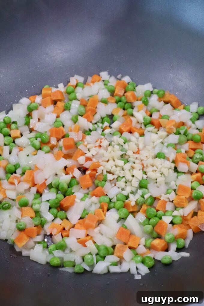 diced onions, carrots, peas and garlic sautéing in a large skillet