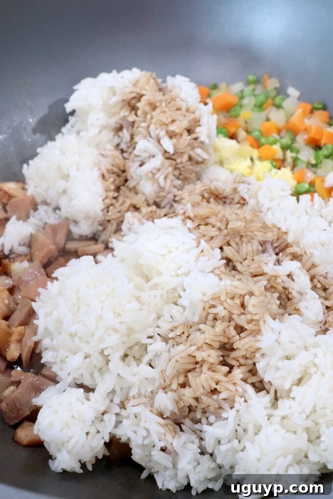 cooked rice in skillet covered with soy sauce and sriracha, ready to be mixed