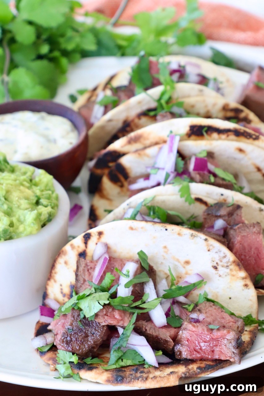 Delicious flat iron steak tacos served on a plate with a side of creamy guacamole, ready to eat.