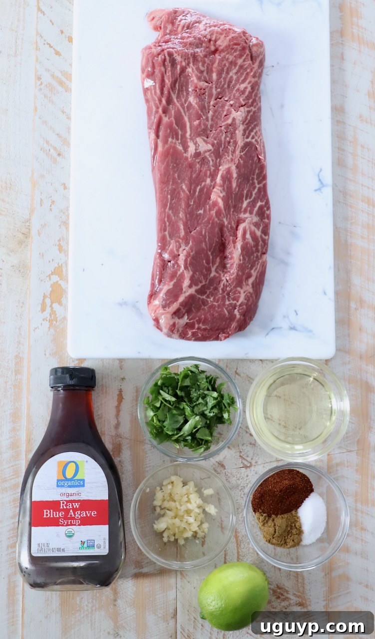 Raw flat iron steak alongside marinade ingredients including lime, oil, agave, spices, and cilantro on a white wooden board.