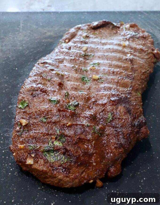 Perfectly grilled flat iron steak resting on a wooden cutting board before slicing.