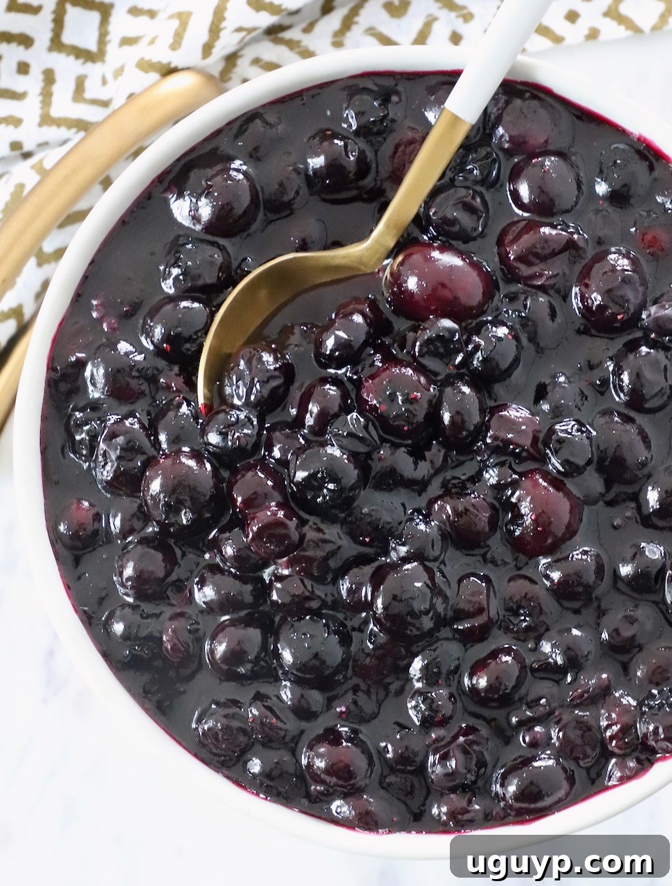 A bowl of vibrant homemade blueberry pie filling with a spoon resting inside, ready for use.