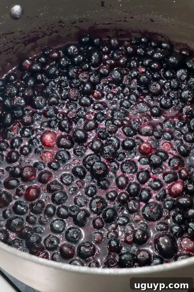 Blueberries simmering in their own liquid with sugar and cornstarch, starting to thicken.