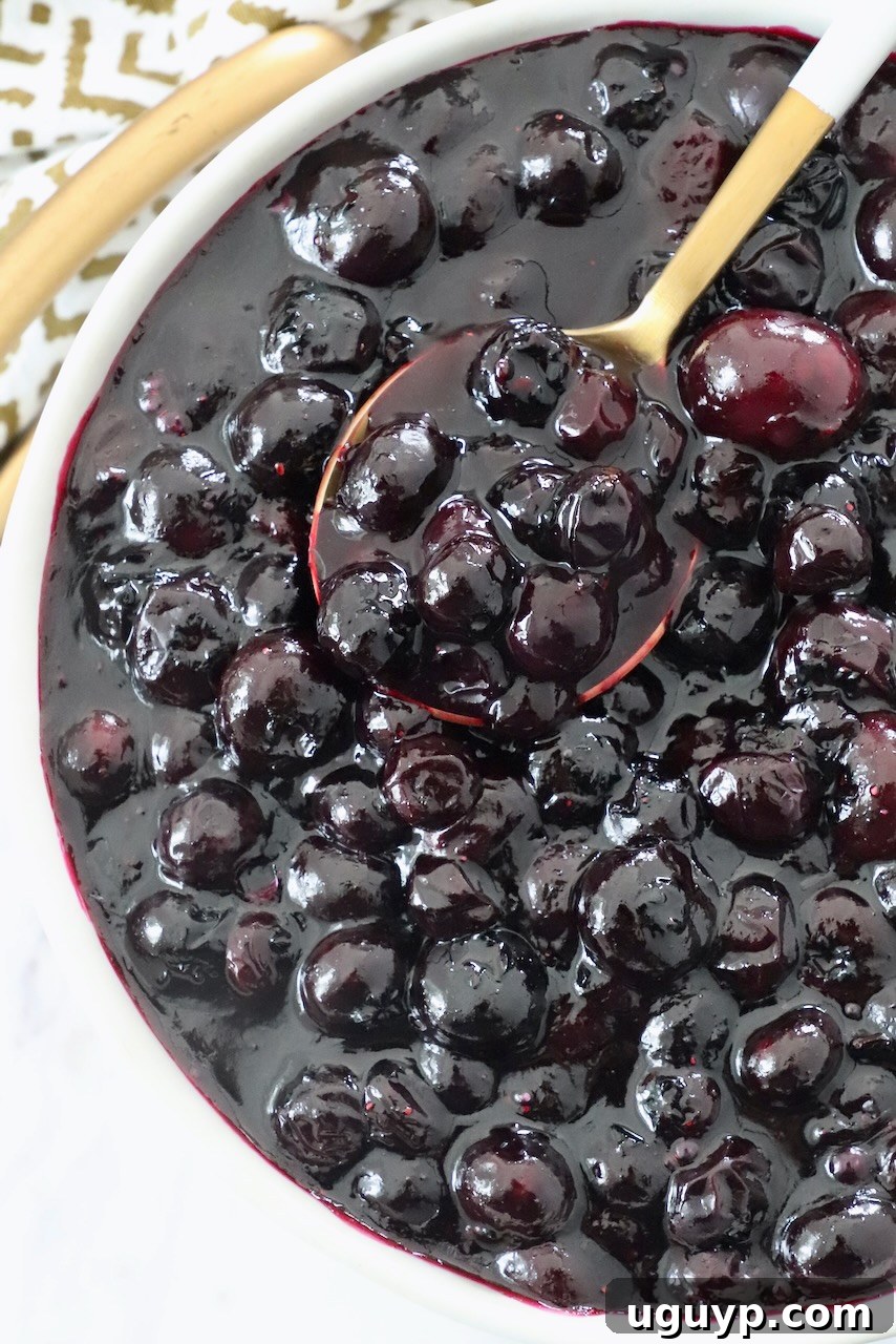 A ceramic bowl filled with glossy homemade blueberry pie filling, with a metal spoon scooping some out.