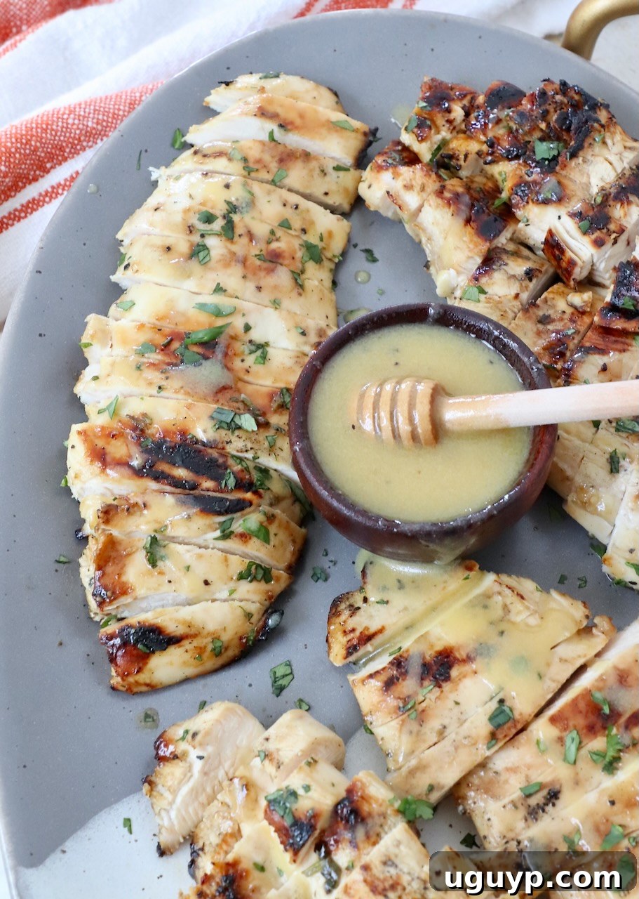 sliced grilled chicken on plate with honey mustard dressing in small bowl next to the chicken