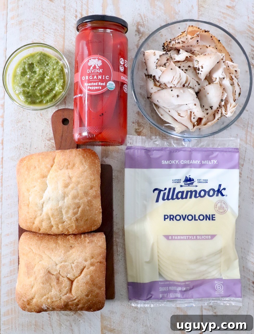 Ingredients for turkey pesto sandwiches laid out on a white wooden board