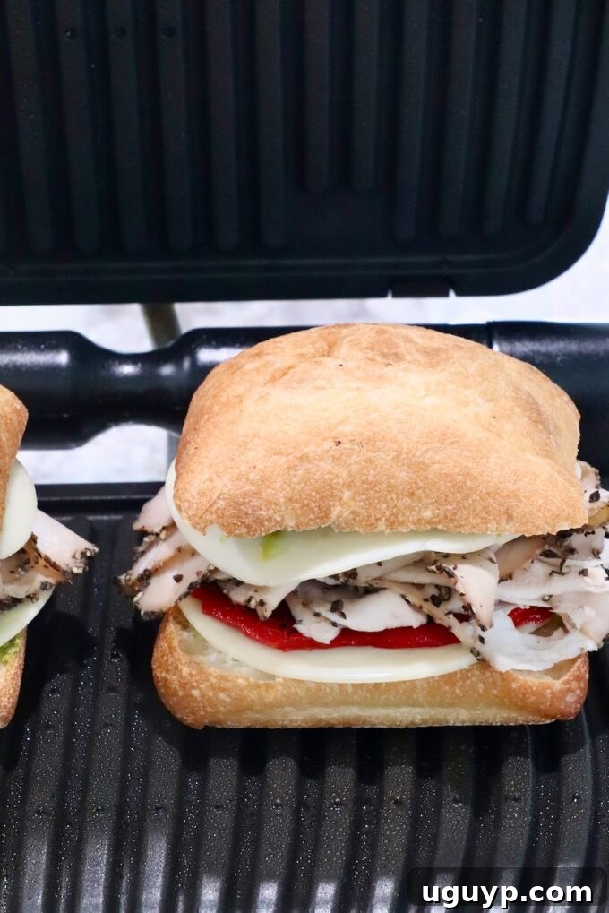 A turkey pesto sandwich cooking inside an indoor grill or panini press