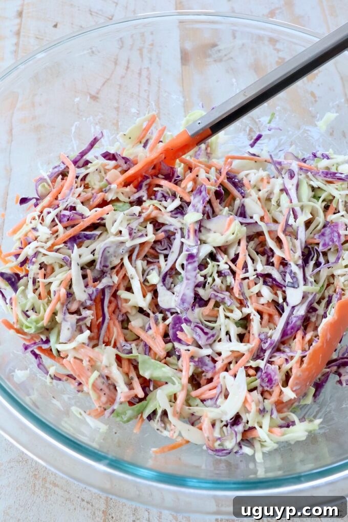 prepared coleslaw in large glass bowl with kitchen tongs