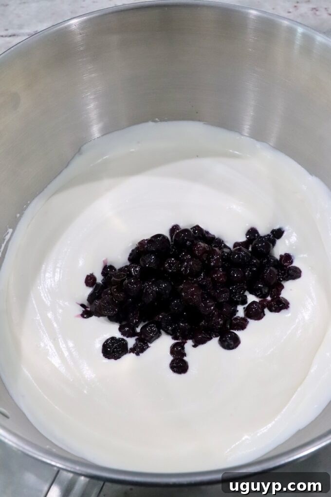 The smooth, creamy ice cream base with swirls of rich blueberry pie filling being gently folded together in a large mixing bowl.