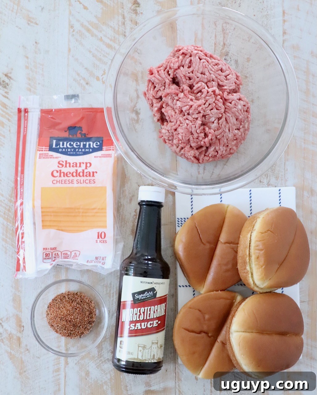 Ingredients for air fryer cheeseburgers laid out on a white wooden board, including ground beef, seasoning, cheese, and buns.