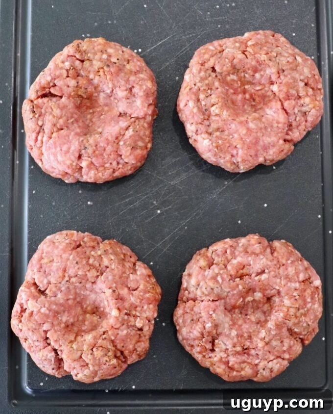 Raw burger patties formed and ready on a cutting board, showing the thumb indentation.