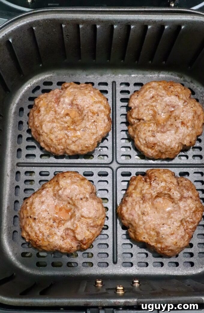 Partially cooked burger patties in the air fryer, showing some browning.