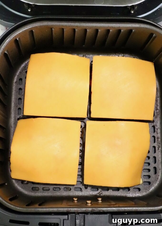 Cooked burger patties topped with slices of cheese, melting in the air fryer.