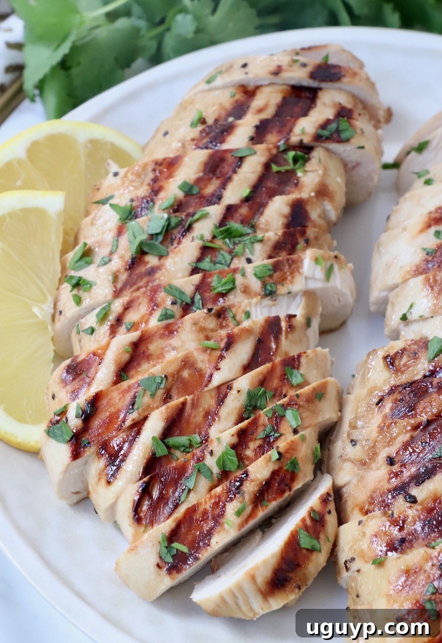 Sliced grilled chicken on a plate with fresh lemon wedges, ready to serve.