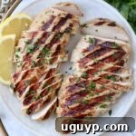 Sliced grilled chicken on plate with lemon wedges