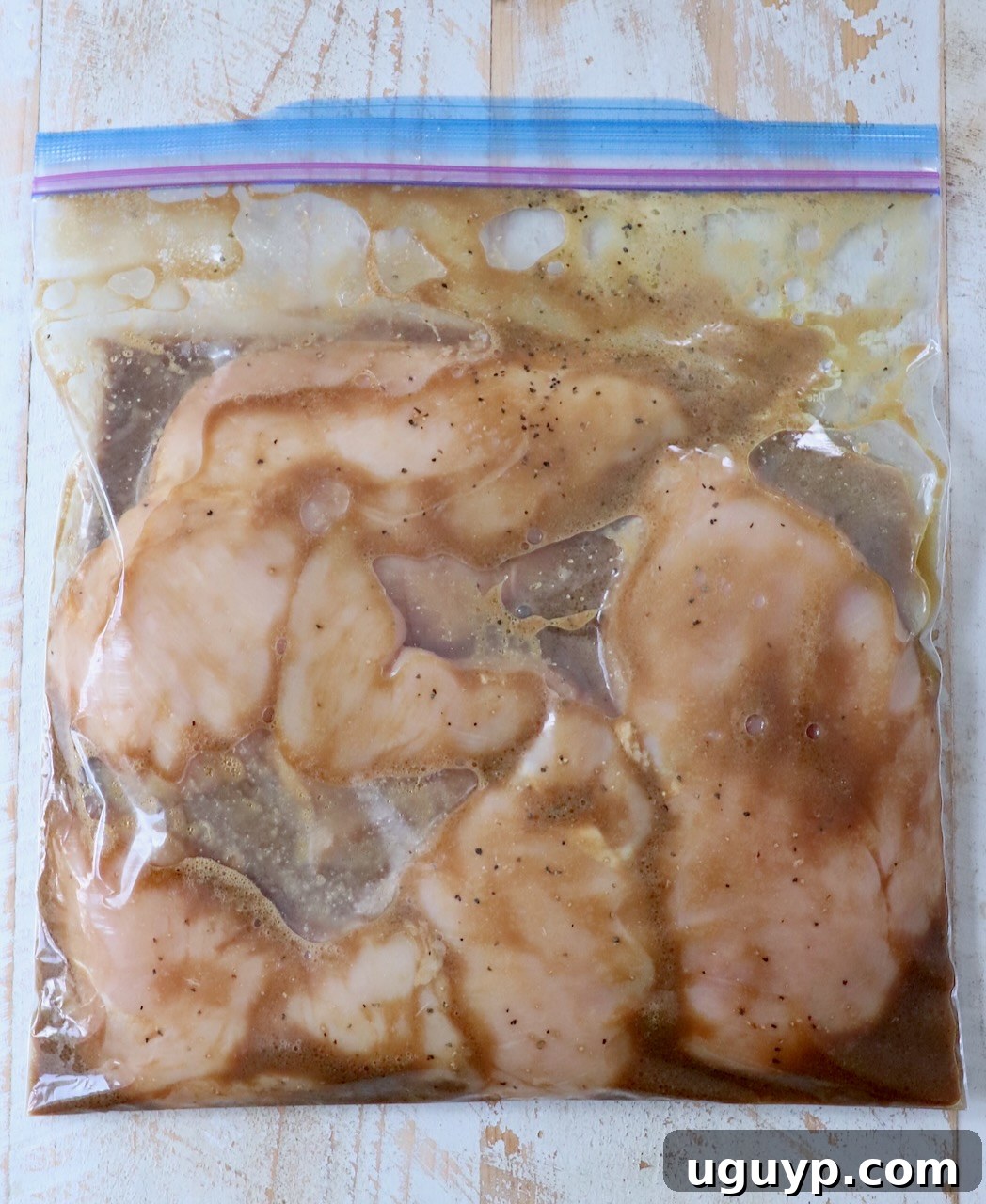 Chicken breasts soaking in the marinade inside a plastic zipper bag.