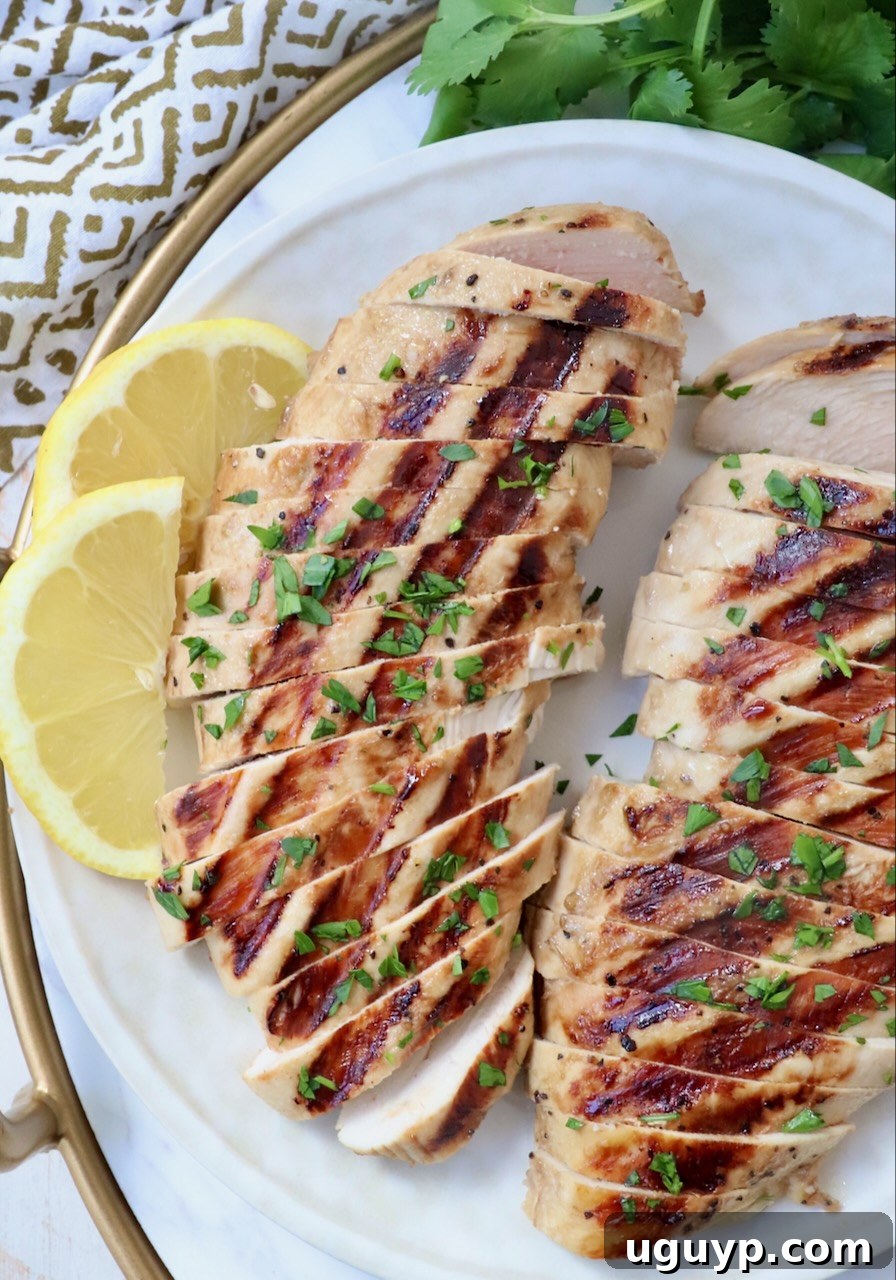 Close-up of perfectly sliced grilled chicken on a plate, garnished with lemon wedges, highlighting its juicy texture.