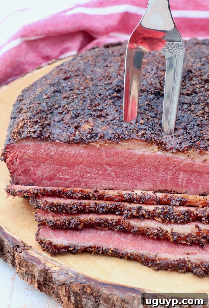 sliced pastrami on a wood board with a meat fork stuck into a piece of pastrami, ready to be served