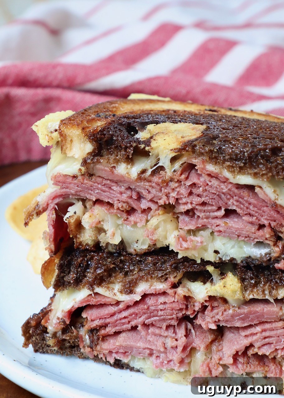 hot pastrami reuben sandwich sliced in half and stacked up on a plate with pickles