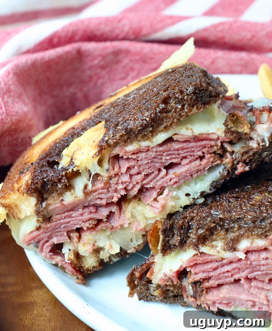 Close-up of a stacked hot pastrami reuben sandwich on a plate, ready to be served.