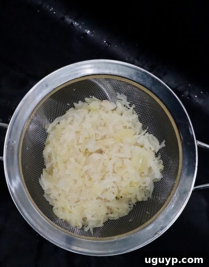 Sauerkraut draining in a fine mesh strainer over a sink, showing excess liquid being removed.