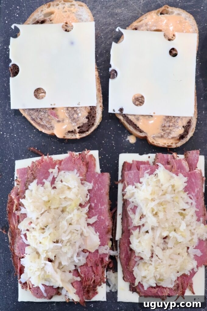 Rye bread slices on a cutting board, with Swiss cheese, sliced pastrami, and drained sauerkraut arranged on top, ready for assembly.
