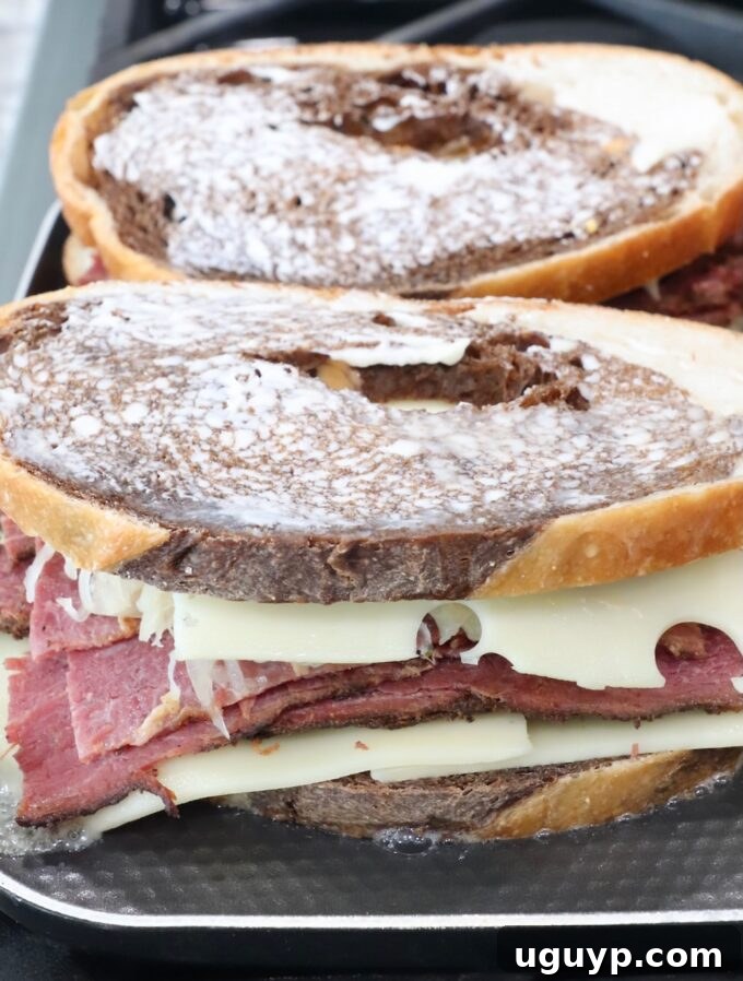 Two uncooked pastrami reuben sandwiches placed on a griddle, ready to be grilled to perfection.