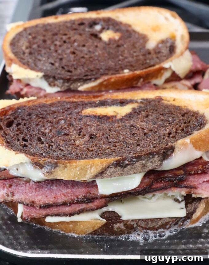 Golden-brown, cooked pastrami reuben sandwiches on a griddle with melted cheese, indicating readiness.