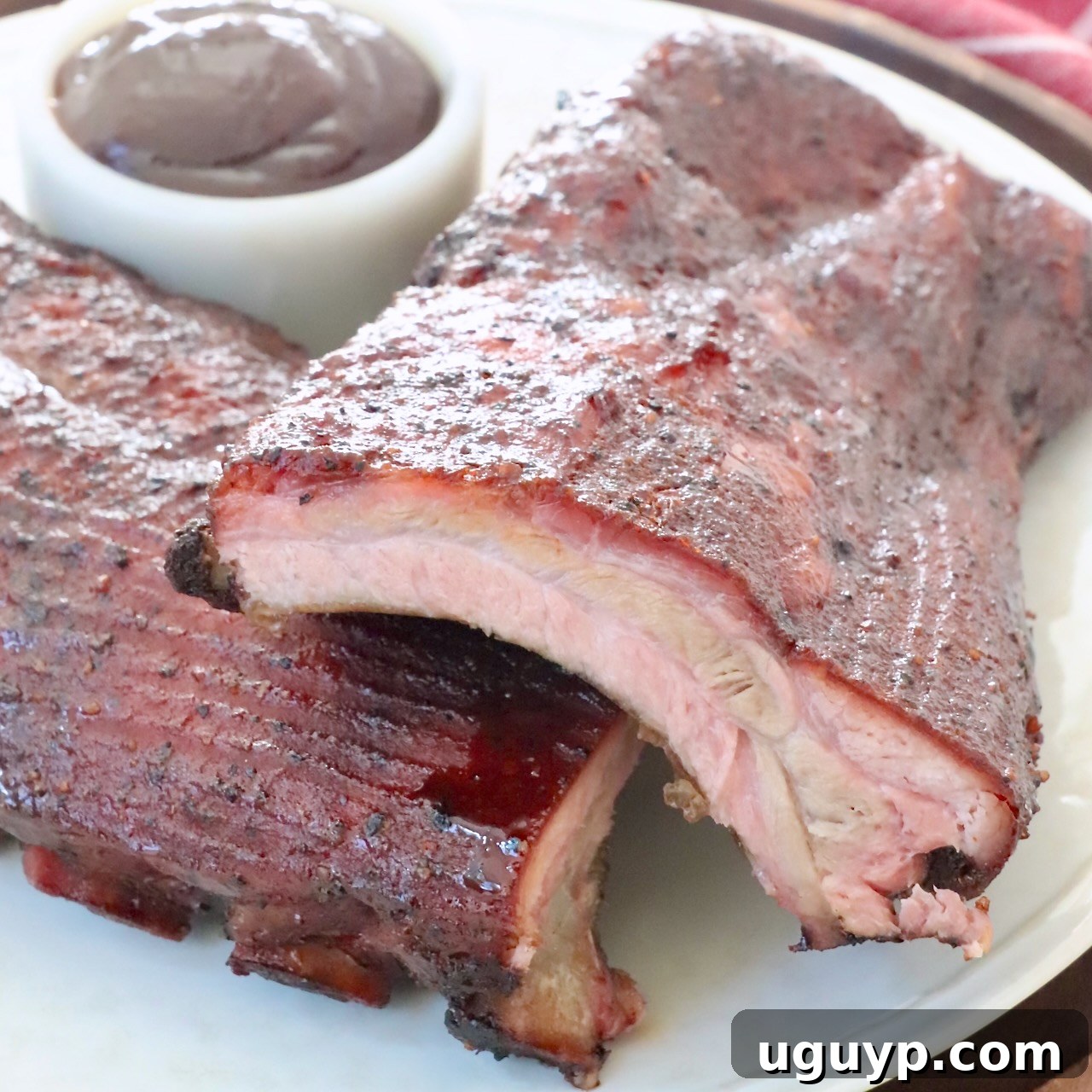A glorious stack of perfectly smoked baby back ribs, glistening with BBQ sauce, arranged on a rustic plate, emphasizing their tender, meaty perfection.