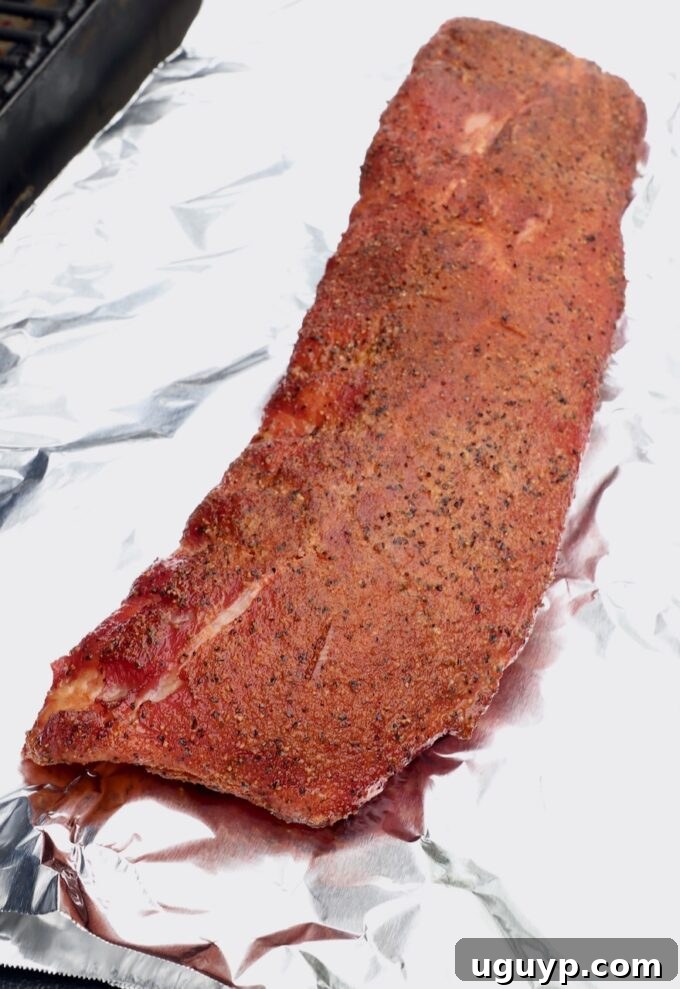 A rack of partially smoked baby back ribs, beautifully browned, sitting on a sheet of heavy-duty aluminum foil inside a smoker, preparing for the wrapping stage.