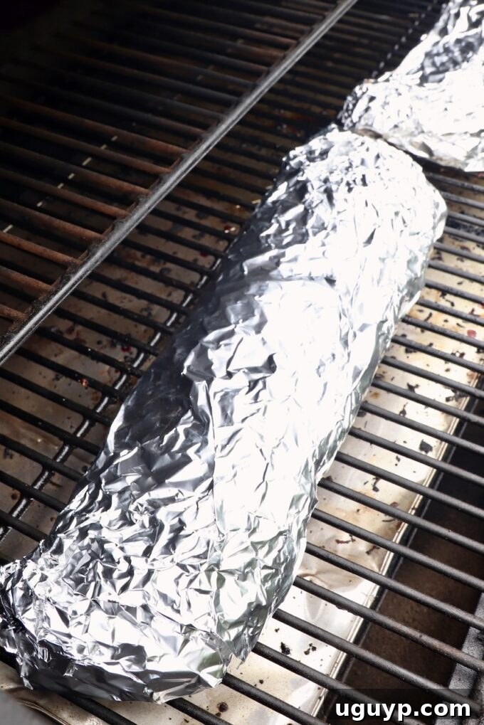 A tightly wrapped rack of baby back ribs in heavy-duty aluminum foil, steaming gently on the smoker, ensuring maximum tenderness.
