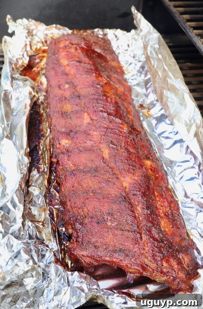 Perfectly sauced and glazed baby back ribs, uncovered and glistening, finishing their final smoke hour on the smoker grates.