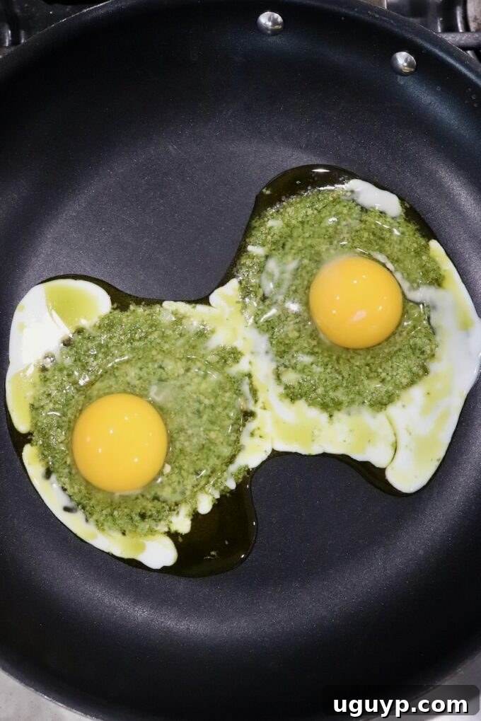 eggs cracked on top of pesto in skillet