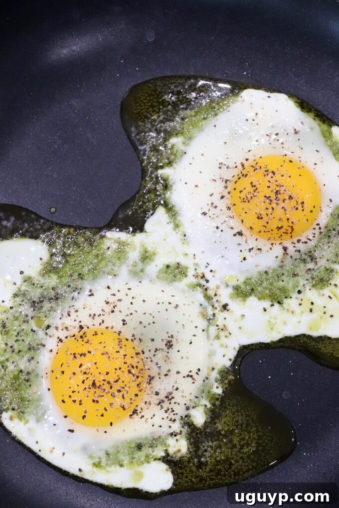 cooked eggs on top of pesto in skillet, seasoned with salt and pepper