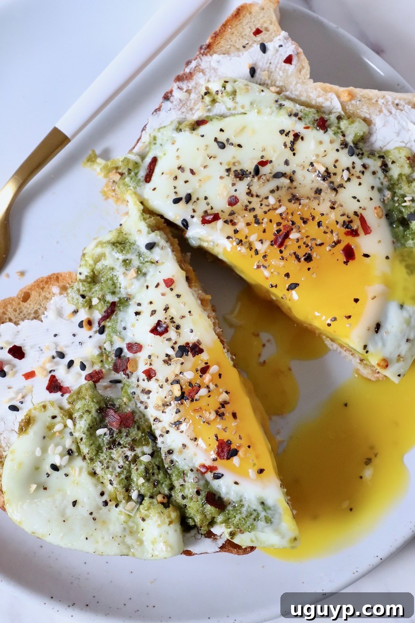 pesto egg on top of toast, sliced in half, on plate