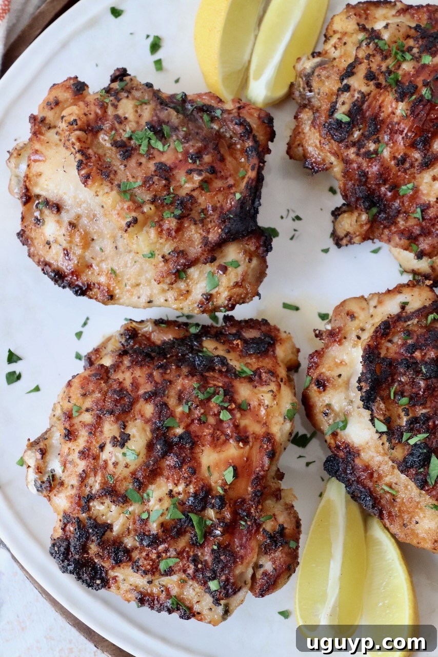 cooked chicken thighs on plate with lemon wedges, garnished with fresh herbs