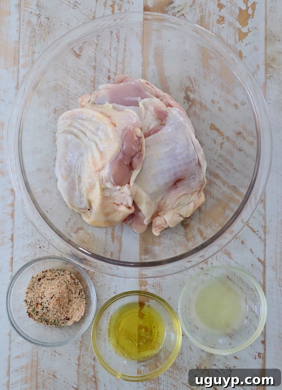 ingredients for air fryer chicken thighs on white wood board, including chicken thighs, olive oil, lemon, and seasoning