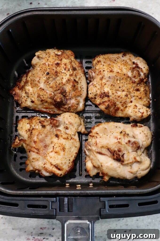 partially cooked bone-in chicken thighs in air fryer basket, after initial cooking phase