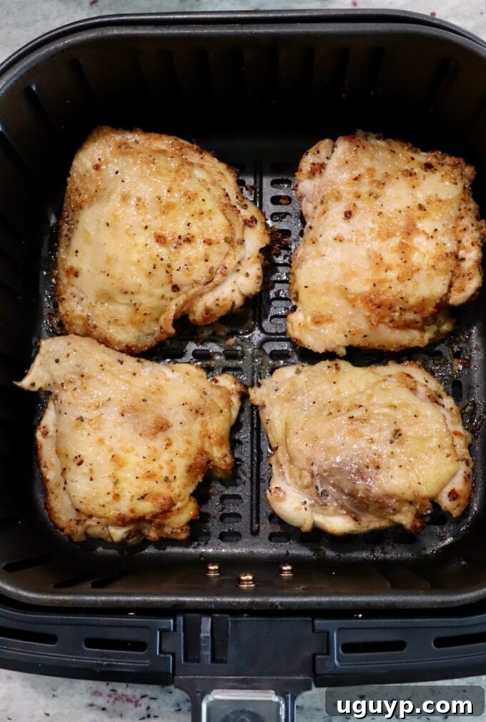 partially cooked bone-in chicken thighs in air fryer basket, flipped to skin-side up