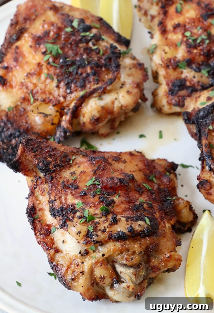 cooked chicken thighs on plate, with a side of fresh parsley and lemon