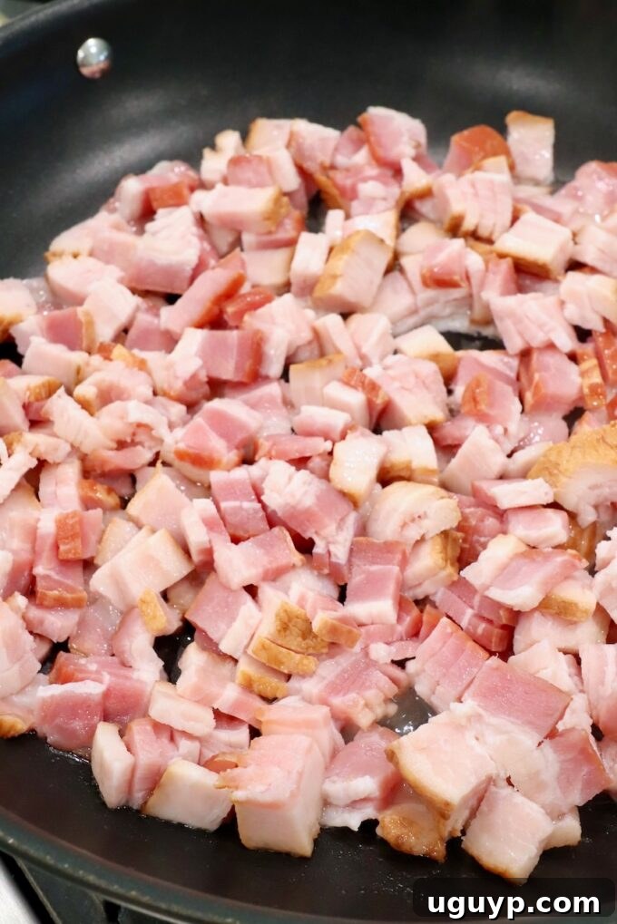 Diced uncooked thick-cut bacon in a large skillet on the stovetop.