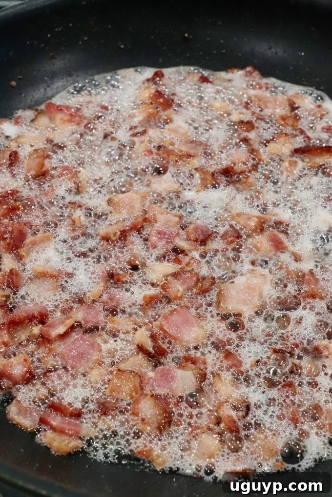 Diced bacon frying and crisping in a hot skillet, rendering its fat.